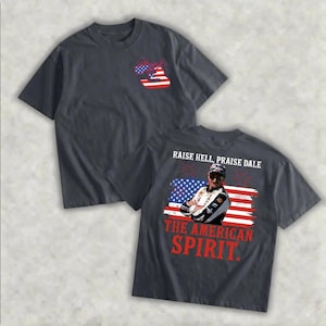 May include: Dark gray t-shirts with patriotic designs. One shirt features a red, white, and blue graphic on the front. The other shirt displays a photo of a man with the text "RAISE HELL, PRAISE DALE" and "THE AMERICAN SPIRIT."