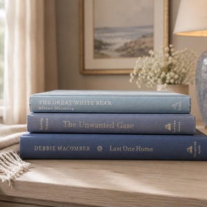 May include: A stack of three hardcover books with blue fabric covers. The top book is titled The Great White Bear by Kieran Mulvaney. The middle book is The Unwanted Gaze by Jeffrey Rosen. The bottom book is Last One Home by Debbie Macomber.