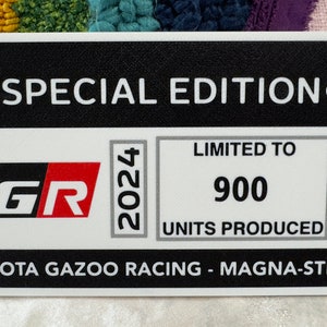 May include: A black and white sticker with the text "SPECIAL EDITION" and the Toyota logo. The sticker also features the text "GR" in red and black, "2024" in gray, "LIMITED TO 900 UNITS PRODUCED" in black and white, and "TOYOTA GAZOO RACING - MAGNA-STEYR" in black.