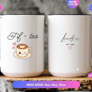 May include: Two white ceramic mugs with black handles and rims. The left mug features the text "Fif - tea" above a cartoon coffee cup with a winking face and three small hearts. The right mug displays the name "Liedka" above "EST: 1986" and a heart.