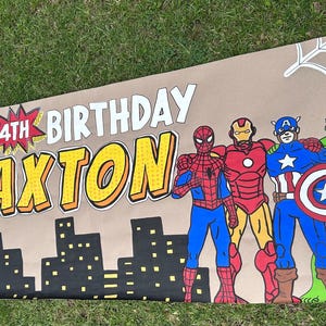 May include: A rectangular banner with a tan background featuring the text "HAPPY 4TH BIRTHDAY BRAXTON" in bold white and yellow letters. The design includes a black city skyline, a white spiderweb, and illustrations of Spider-Man, Iron Man, Captain America, and the Hulk.