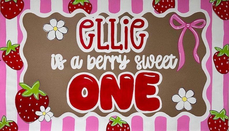 May include: A rectangular sign with a pink and white striped border featuring red strawberries and white flowers. The center is brown with the text GLLIG is a berry sweet ONE in red and white lettering, accented by a pink bow on the right side.