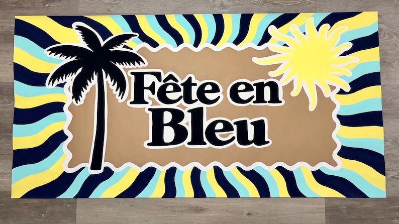 May include: A rectangular sign featuring a wavy, sunburst pattern in navy blue, light blue, and yellow. Centered is a tan, scalloped-edge rectangle with the text "F&ecirc;te en Bleu" in black, flanked by a black palm tree silhouette and a yellow sun.