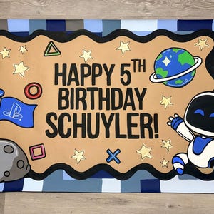 May include: A rectangular banner with a blue pixelated border featuring the text HAPPY 5TH BIRTHDAY SCHUYLER! in black. The design includes a grey moon with a blue flag, a cartoon robot, a planet with rings, and various yellow geometric shapes.