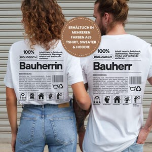 Könnte beinhalten: Zwei Personen tragen weiße T-Shirts mit deutschem Text. Die Shirts tragen die Aufschrift "Bauherrin" und "Bauherr" mit zusätzlichem Text und Symbolen. Die Shirts sind mit "100% BIOLOGISCH" gekennzeichnet und als T-Shirt, Pullover und Hoodie erhältlich.