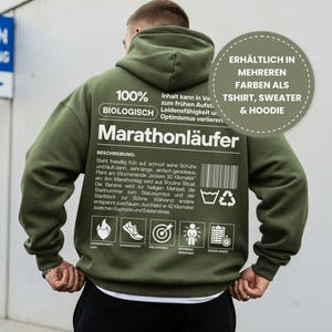 Könnte beinhalten: Olivgrüner Kapuzenpullover mit dem deutschen Wort "Marathonläufer" auf dem Rücken. Der Hoodie hat weißen Text und Grafiken, darunter einen Barcode und Waschanweisungen. Der Text gibt auch an, dass der Hoodie in mehreren Farben als T-Shirt, Pullover und Hoodie erhältlich ist.
