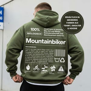 Könnte beinhalten: Olivgrüner Mountainbiker-Hoodie mit weißem Text und Grafiken. Auf der Rückseite des Hoodies stehen die Worte "Mountainbiker" und eine Beschreibung auf Deutsch. Der Hoodie hat auch eine Grafik mit der Aufschrift "Erhältlich in mehreren Farben als T-Shirt, Sweater & Hoodie."