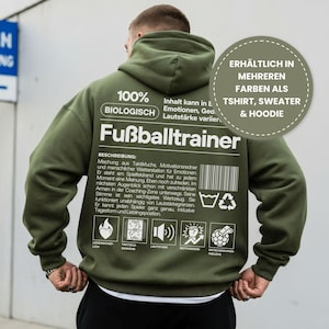 Könnte beinhalten: Ein olivgrüner Hoodie mit weißem Text, der "Fußballtrainer" und anderen deutschen Text liest. Der Hoodie hat auch eine Grafik mit der Aufschrift "100% BIOLOGISCH". Eine kreisförmige Grafik besagt "ERHÄLTLICH IN MEHREREN FARBEN ALS TSHIRT, SWEATER & HOODIE."