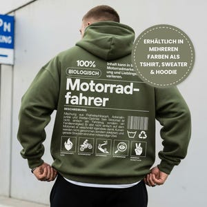 Könnte beinhalten: Olivgrüner Kapuzenpullover mit dem deutschen Text "Motorradfahrer" und weiterem Text. Der Kapuzenpullover hat auch eine Grafik und die Worte "100% BIOLOGISCH". Erhältlich in mehreren Farben als T-Shirt, Pullover und Hoodie.
