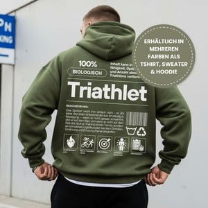 Könnte beinhalten: Olivgrüner Hoodie mit dem Wort "Triathlet" in Weiß auf dem Rücken. Der Hoodie enthält auch Text und Symbole, die sich auf den Triathlonsport beziehen. Erhältlich in mehreren Farben als T-Shirt, Pullover und Hoodie.