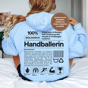 Könnte beinhalten: Hellblauer Hoodie mit dem Aufdruck "Handballerin" auf dem Rücken. Das Design enthält Text und Icons zum Handball, wie einen Ball, eine rennende Figur und eine Trophäe. Erhältlich in mehreren Farben als T-Shirt, Sweater & Hoodie.