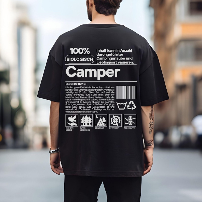 May include: Black t-shirt with white text and graphics. The shirt features the word "Camper" and text in German. The design includes icons related to nature and camping. The shirt is made of a soft material.