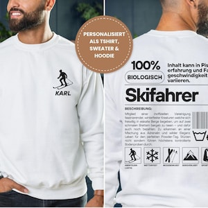 Könnte beinhalten: Ein weißes Langarm-Sweatshirt mit einer schwarzen Skifahrer-Grafik und dem Namen KARL auf der Vorderseite. Die Rückseite zeigt eine große schwarze Grafik, die einem Produktetikett ähnelt, mit dem Text Skifahrer, 100% BIOLOGISCH und verschiedenen Symbolen.
