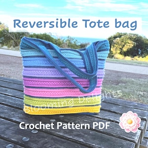 Può includere: Una borsa tote in crochet a righe colorate con un design reversibile. La borsa è realizzata con una varietà di colori vivaci, tra cui blu, viola, rosa, giallo e verde. La borsa è appoggiata su una panchina di legno con un fiore nell'angolo dell'immagine. Il testo "Reversible Tote bag" e "Crochet Pattern PDF" è visibile nell'immagine.