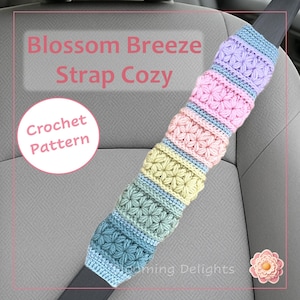 May include: A colorful, crocheted strap cozy with the text "Blossom Breeze Strap Cozy" and "Crochet Pattern." The cozy features a floral design in pastel colors, including pink, blue, yellow, and purple. The cozy is designed to fit over a car seat belt.