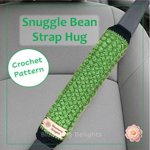 May include: A green crocheted seat belt cover, labeled "Snuggle Bean Strap Hug" and "Crochet Pattern." The cover is made of textured green yarn with black trim. A small tag reads "Blooming Delights."