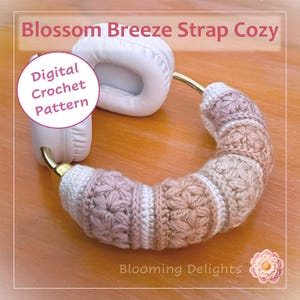 Può includere: Una copertura all'uncinetto per archetto di cuffie con un motivo a punto stella testurizzato nei toni del bianco, beige e rosa polvere. Il testo Blossom Breeze Strap Cozy e Digital Crochet Pattern sono visibili. Il marchio Blooming Delights è incluso.