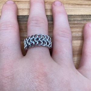 May include: A silver chainmail ring worn on a finger.