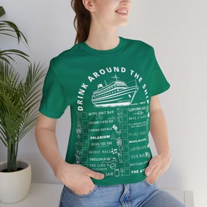 May include: A green t-shirt with the text "DRINK AROUND THE SHIP" and a graphic of a cruise ship. Below the text are check boxes with bar names like "Casino Royale" and "Pesky Parrot". The shirt is made of a soft material.