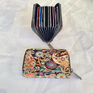 May include: Two zippered card wallets. One wallet is open, displaying multiple cards. The closed wallet features a black background with a colorful paisley pattern in shades of red, blue, orange, and yellow. Both wallets have silver zippers.