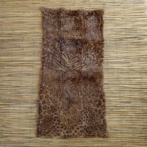 May include: A rectangular rug with a faux animal print design. The rug features a mix of leopard spots and tiger stripes in shades of brown and tan. The rug is placed on a light brown bamboo mat.