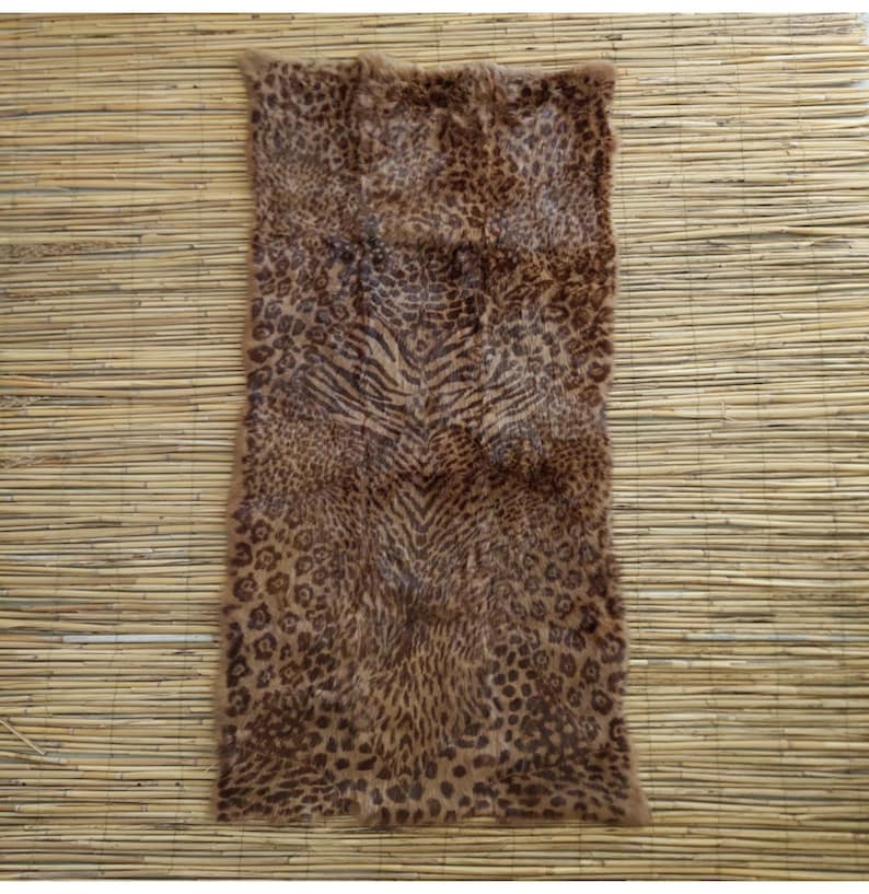 May include: A rectangular rug with a faux animal print design. The rug features a mix of leopard spots and tiger stripes in shades of brown and tan. The rug is placed on a light brown bamboo mat.