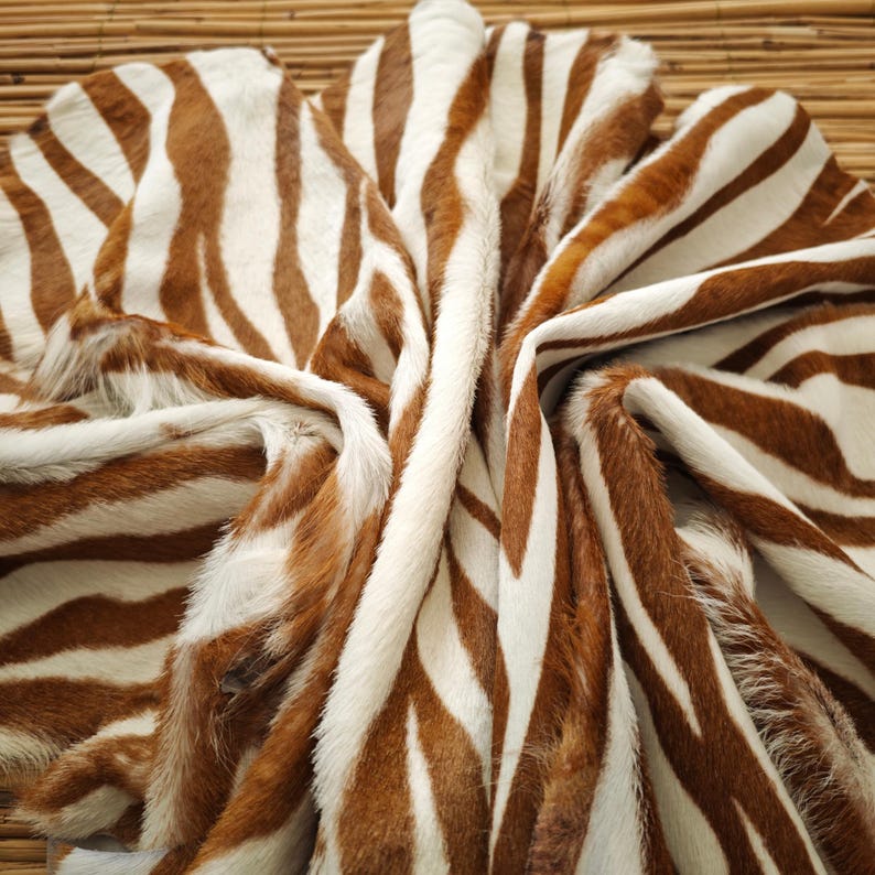 May include: A folded zebra hide with brown and white stripes. The hide has a soft, furry texture and is arranged in a flowing pattern. The natural colors and pattern create a striking visual.