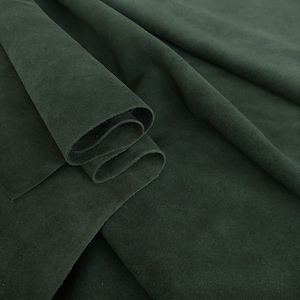 May include: A close-up of a dark green suede fabric, folded and draped. The fabric has a soft, velvety texture.