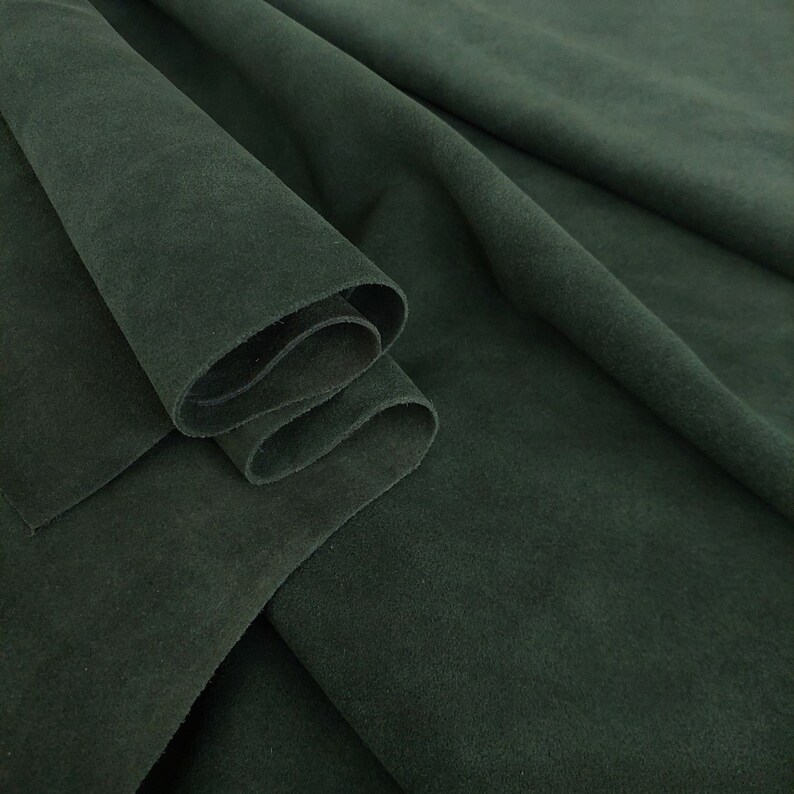 May include: A close-up of a dark green suede fabric, folded and draped. The fabric has a soft, velvety texture.