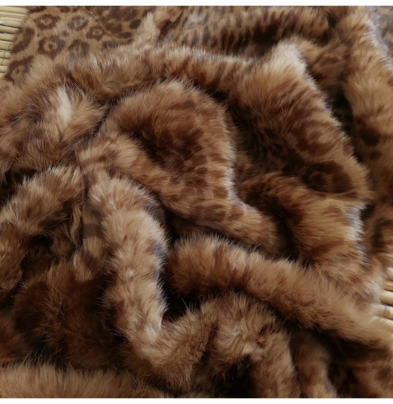 May include: A close-up of a brown faux fur blanket with a leopard print design. The blanket has a soft, plush texture and is folded, creating shadows and depth. The color palette is warm, with shades of brown and tan.