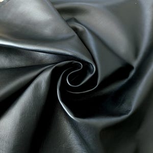 May include: Close-up of a swatch of black leather fabric. The material is smooth and shiny, with subtle variations in texture. The fabric is draped and folded, creating shadows and highlights that emphasize its supple quality. Ideal for upholstery, clothing, or accessories.