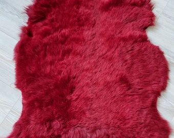 Può includere: Un tappeto in pelle di pecora rosso scuro con una texture morbida e soffice.