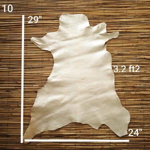 May include: A beige leather hide, approximately 29 inches long and 24 inches wide, with a surface area of 3.2 square feet. The hide has irregular edges and a natural, textured appearance. The hide is displayed on a bamboo mat.