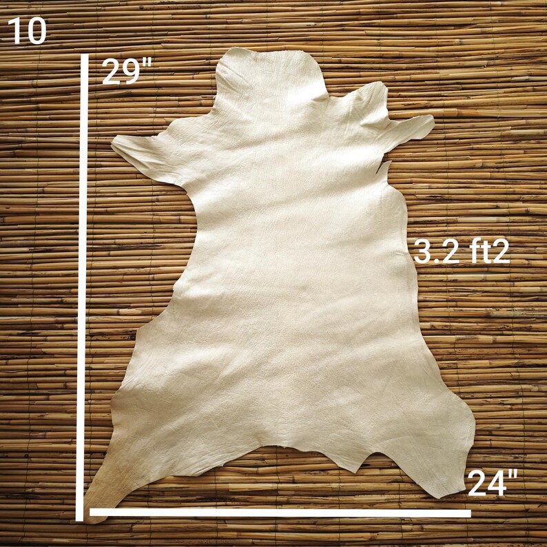May include: A beige leather hide, approximately 29 inches long and 24 inches wide, with a surface area of 3.2 square feet. The hide has irregular edges and a natural, textured appearance. The hide is displayed on a bamboo mat.