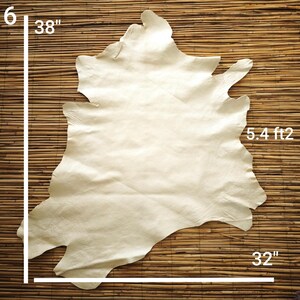 May include: A cream-colored leather hide, approximately 38 inches long and 32 inches wide, with a surface area of 5.4 square feet. The hide is irregularly shaped and rests on a bamboo mat.