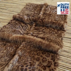 May include: A brown and tan faux fur rug with a leopard and zebra print design. The rug has a soft, plush texture and a border of fluffy fur. The rug is displayed on a light brown woven surface. The image includes a "DUTY FREE" sticker.