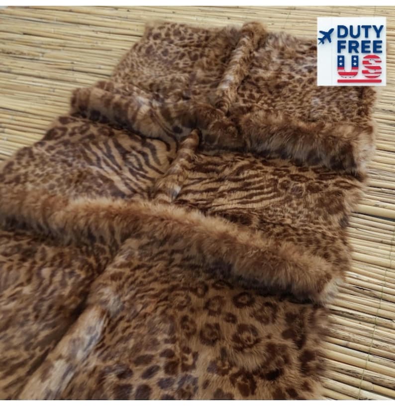 May include: A brown and tan faux fur rug with a leopard and zebra print design. The rug has a soft, plush texture and a border of fluffy fur. The rug is displayed on a light brown woven surface. The image includes a "DUTY FREE" sticker.