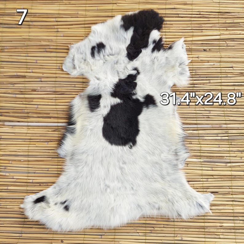 May include: A cowhide rug with a white background and black spots. The rug measures 31.4" x 24.8". The number 7 is in the upper left corner. The rug is on a bamboo mat.