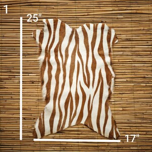 May include: A cowhide rug with a zebra stripe pattern in brown and white. The rug measures 25 inches by 17 inches.
