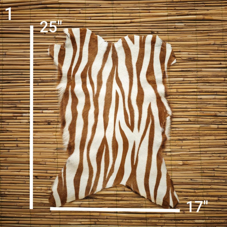 May include: A cowhide rug with a zebra stripe pattern in brown and white. The rug measures 25 inches by 17 inches.