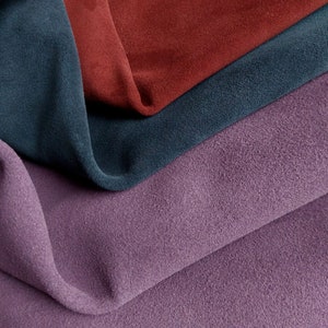 May include: Close-up of four fabric swatches in different colours and textures. The swatches are folded and layered on top of each other. The top swatch is a deep red, the second is a dark teal, the third is a light purple, and the bottom is a darker purple.