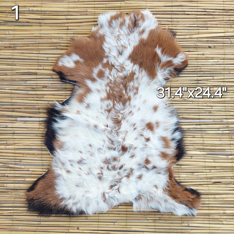 May include: A cowhide rug with a natural pattern of brown, white, and black. The rug measures 31.4 inches by 24.4 inches. The hide has a soft, textured appearance and is displayed on a bamboo mat.