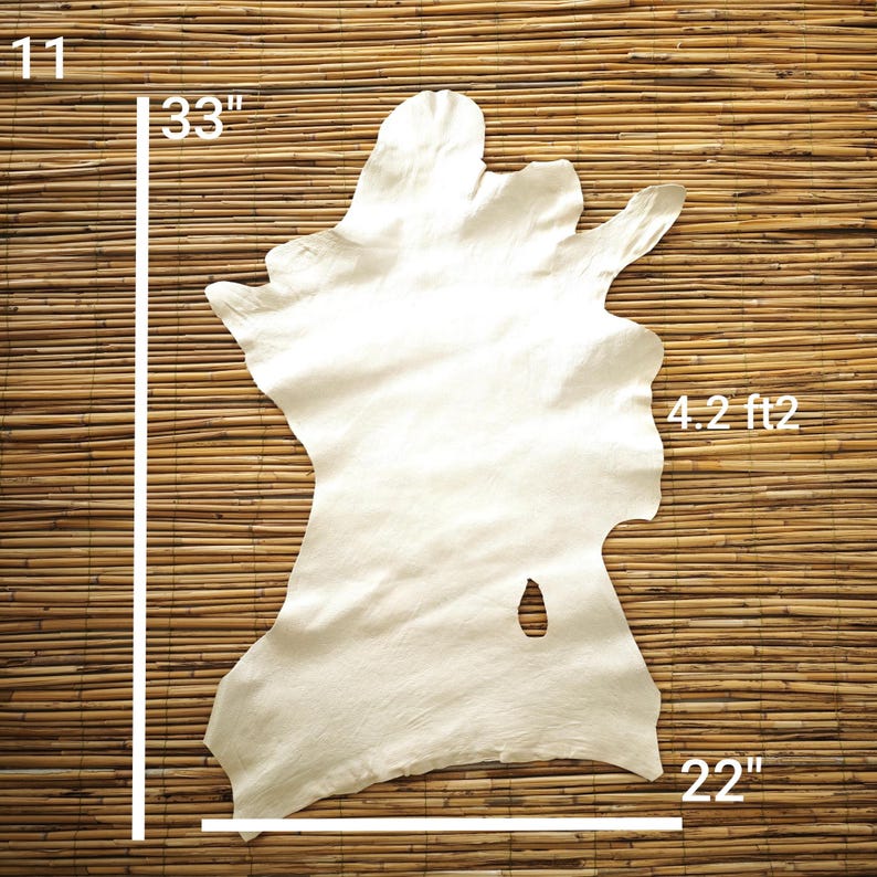 May include: Off-white leather hide with irregular edges, measuring 33 inches long and 22 inches wide. The hide has a surface area of 4.2 square feet. The background is a natural bamboo mat.