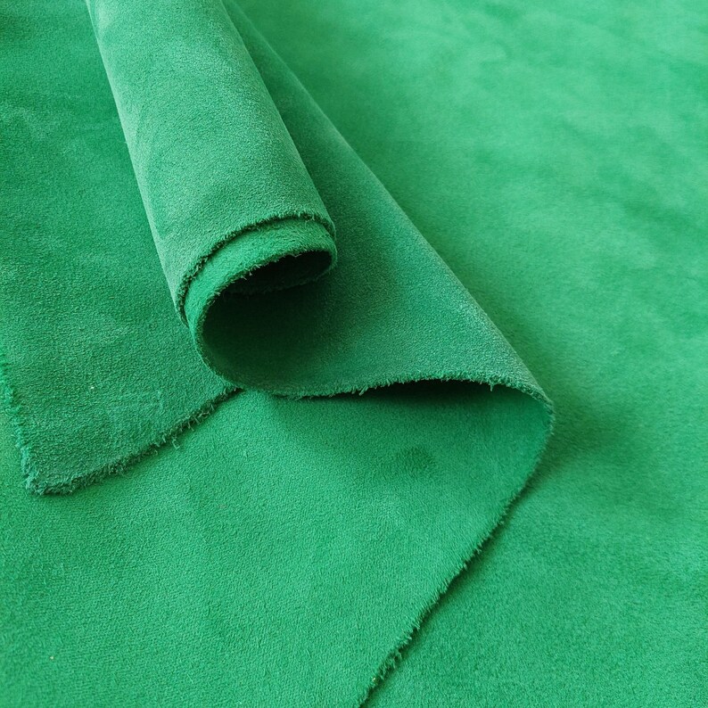 May include: A close-up of a green suede fabric, folded and rolled, showing the texture and softness of the material.