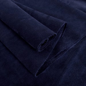Könnte beinhalten: Nahaufnahme eines gefalteten Stücks marineblauen Stoffes. Der Stoff hat eine weiche, samtige Textur und scheint ein schweres Material zu sein. Die Kanten des Stoffes sind leicht ausgefranst, und die Falten erzeugen Schatten und Tiefe.