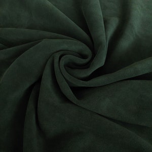 May include: A close-up of a dark green fabric with a soft, velvety texture. The fabric is folded and draped, creating a smooth, flowing surface.