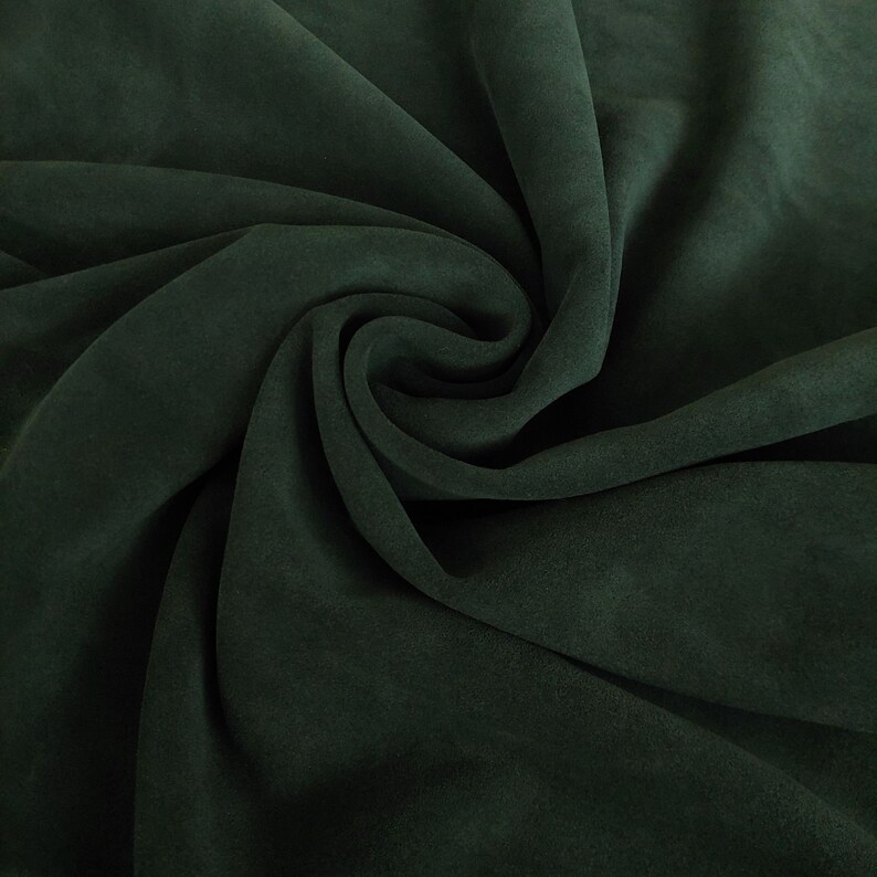 May include: A close-up of a dark green fabric with a soft, velvety texture. The fabric is folded and draped, creating a smooth, flowing surface.