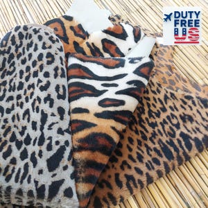 Puede incluir: Surtido de telas de piel sintética con estampados de animales, incluyendo patrones de leopardo y tigre. Las telas muestran una variedad de colores, incluyendo marrón, negro y beige. Las telas están dispuestas sobre una estera de bambú.