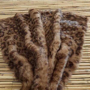 May include: A brown faux fur throw blanket with a leopard print pattern. The blanket is folded, showing the soft texture and varying shades of brown. The throw is displayed on a bamboo mat.