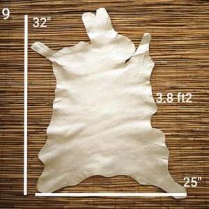May include: Off-white leather hide, approximately 32 inches by 25 inches, with a surface area of 3.8 square feet. The hide has an irregular shape and is displayed against a bamboo background. The image shows the dimensions of the hide.
